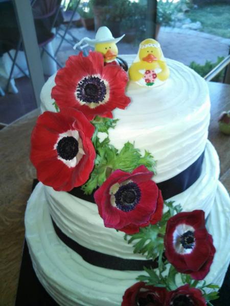 This is a whimsical wedding cake decorated with lovely poppies and yellow ducks as the cake topper.